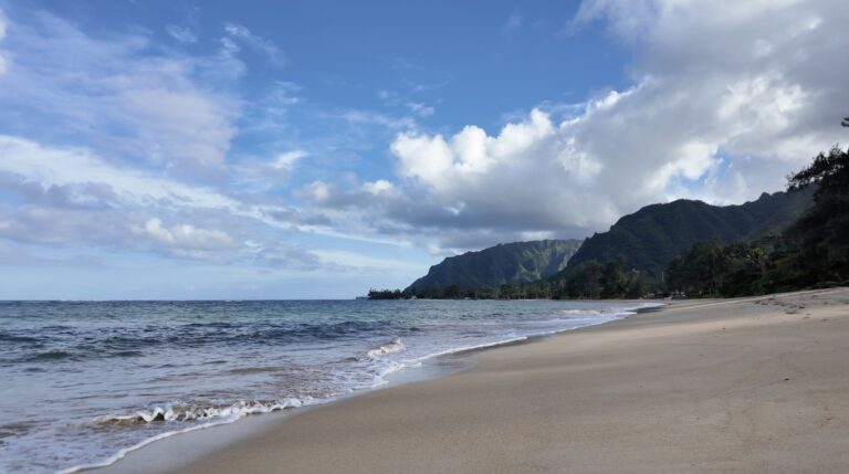 A pristine empty beach with calm turquoise waves and island mountains in the background
